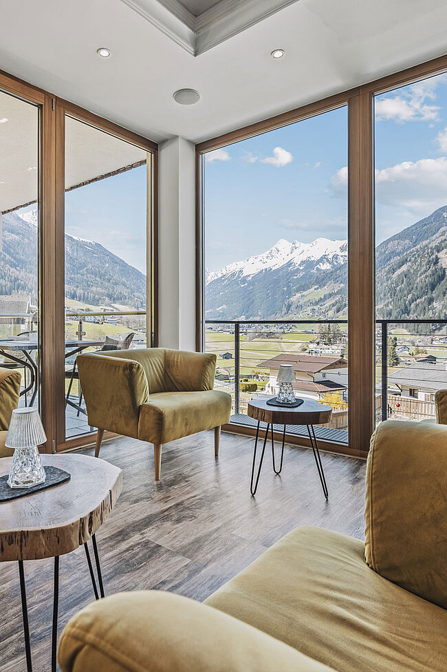Moderne Lounge mit senffarbenen Sesseln, kleinen Tischen und großen Fenstern mit Blick auf eine malerische Berglandschaft.