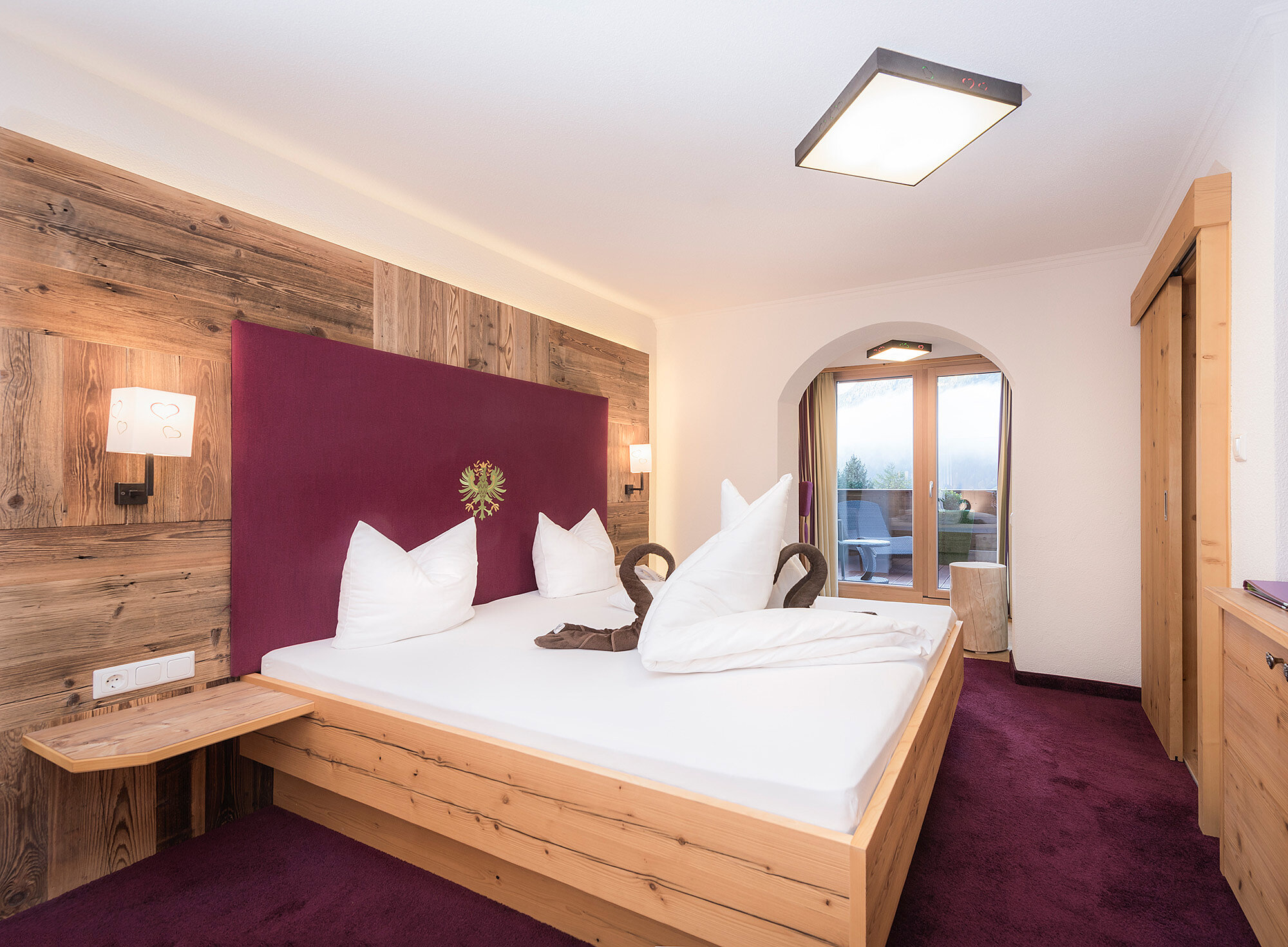 Modernes Hotelzimmer mit großem Bett, Holzakzenten, lila Teppich und einem Fenster mit malerischer Aussicht.