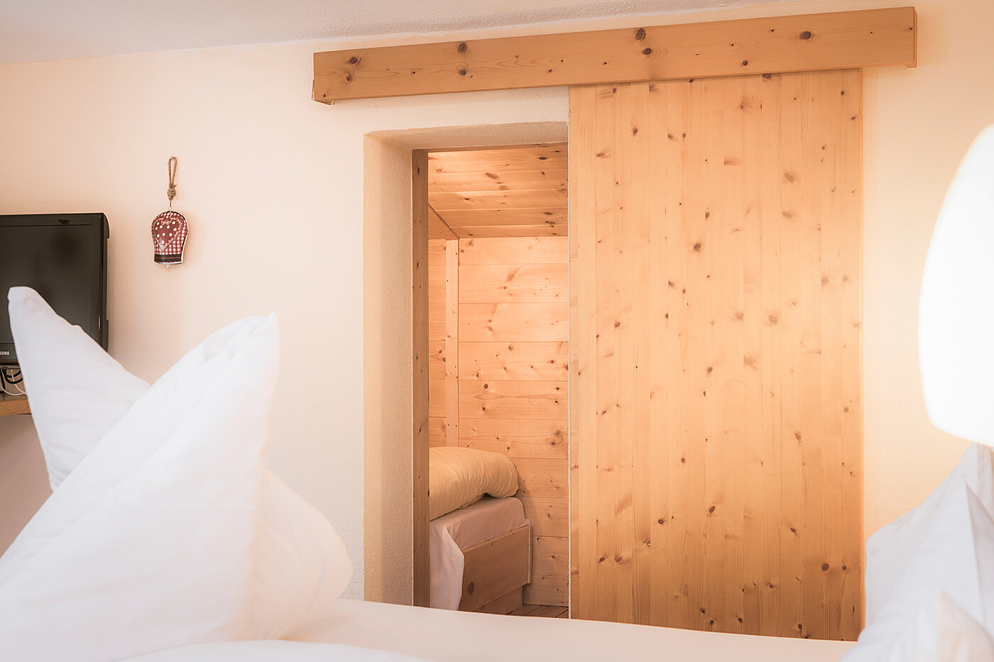 Gemütliches Schlafzimmer mit weißer Bettwäsche und einer Holzschiebetür, die zu einem anderen Zimmer mit Holzwänden und einem Bett führt.