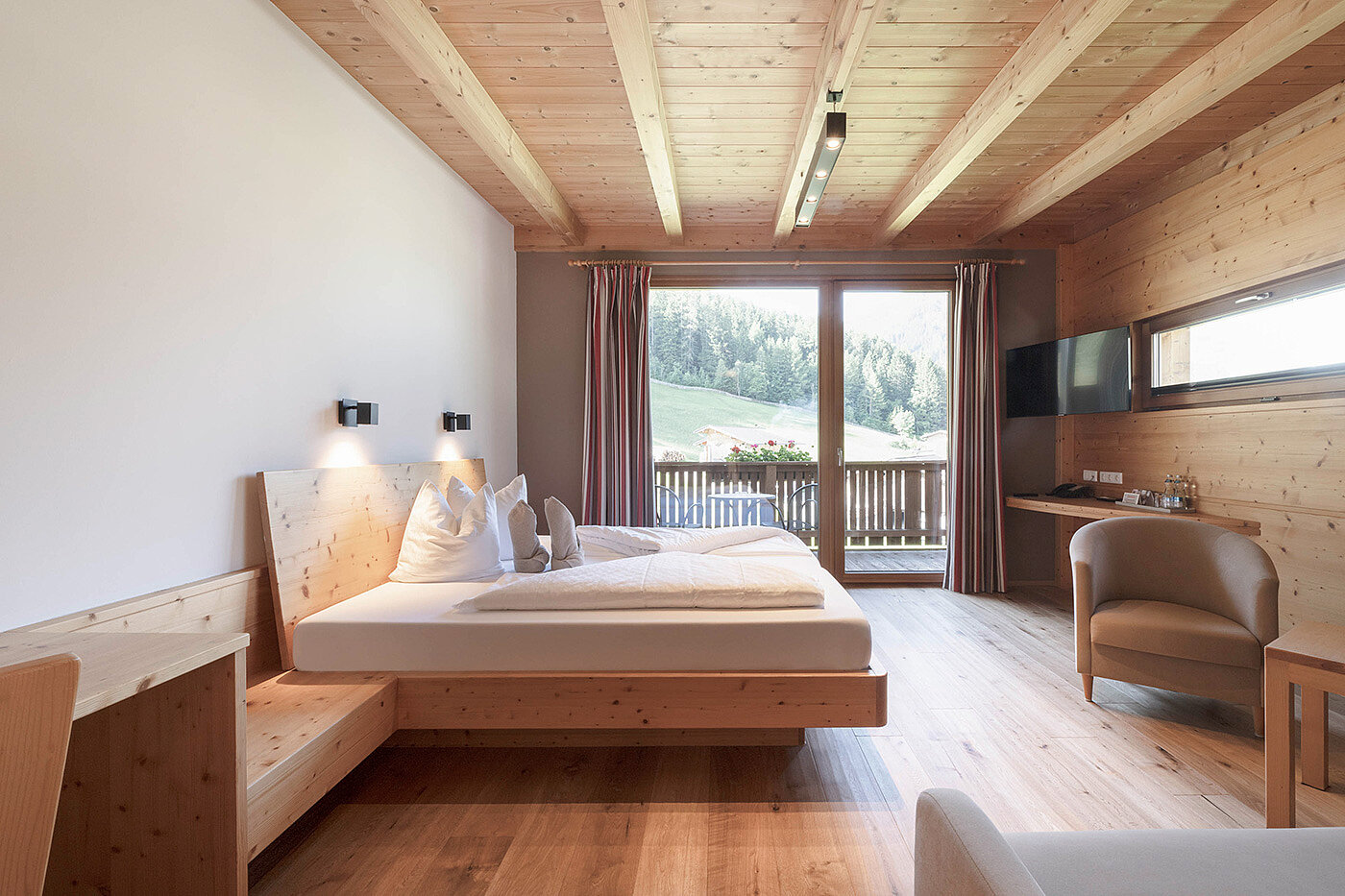 Modernes Hotelzimmer aus Holz mit Doppelbett, Stühlen, Schreibtisch und Balkon mit Blick auf eine grüne Landschaft.