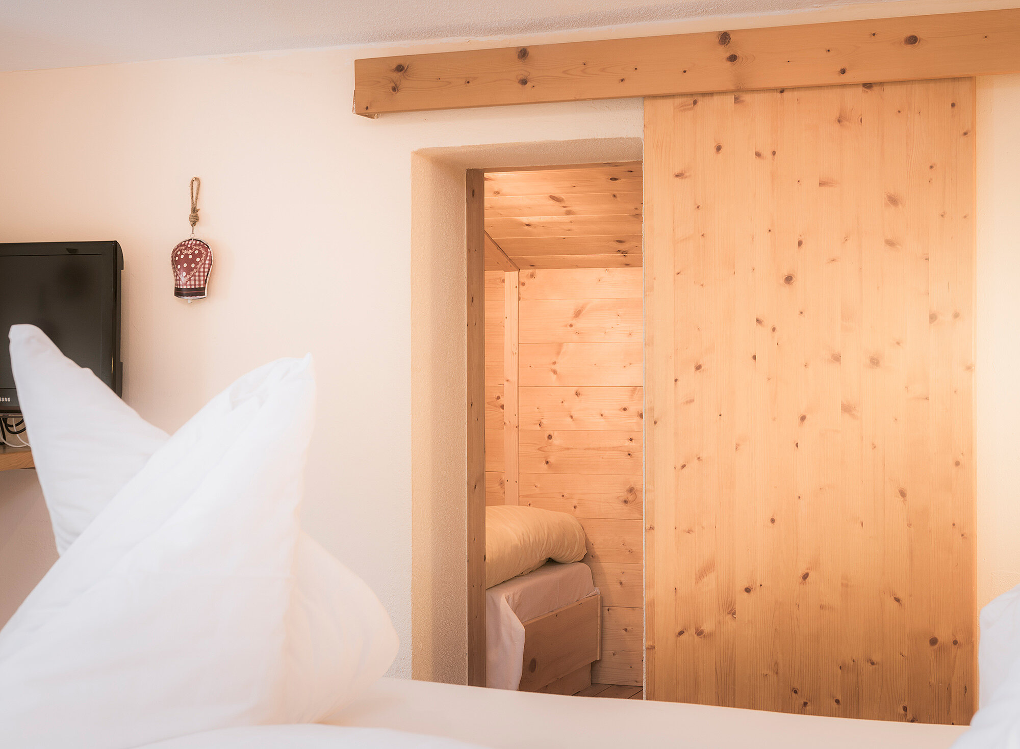 Gemütliches Zimmer mit weißer Bettwäsche, Holzschiebetür und Blick in einen weiteren holzgetäfelten Raum.