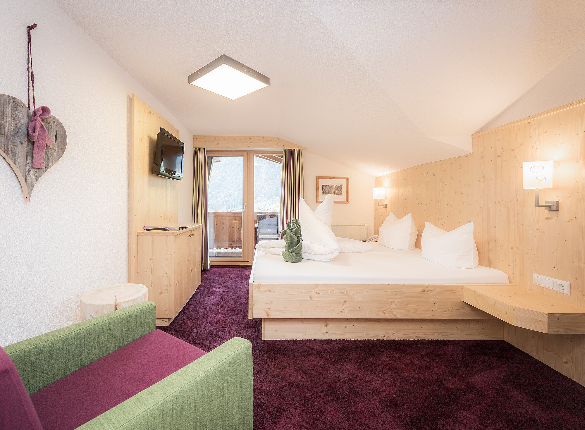 Modernes Hotelzimmer mit Doppelbett, grünem Sessel, Wandfernseher und Balkon mit Glastüren.