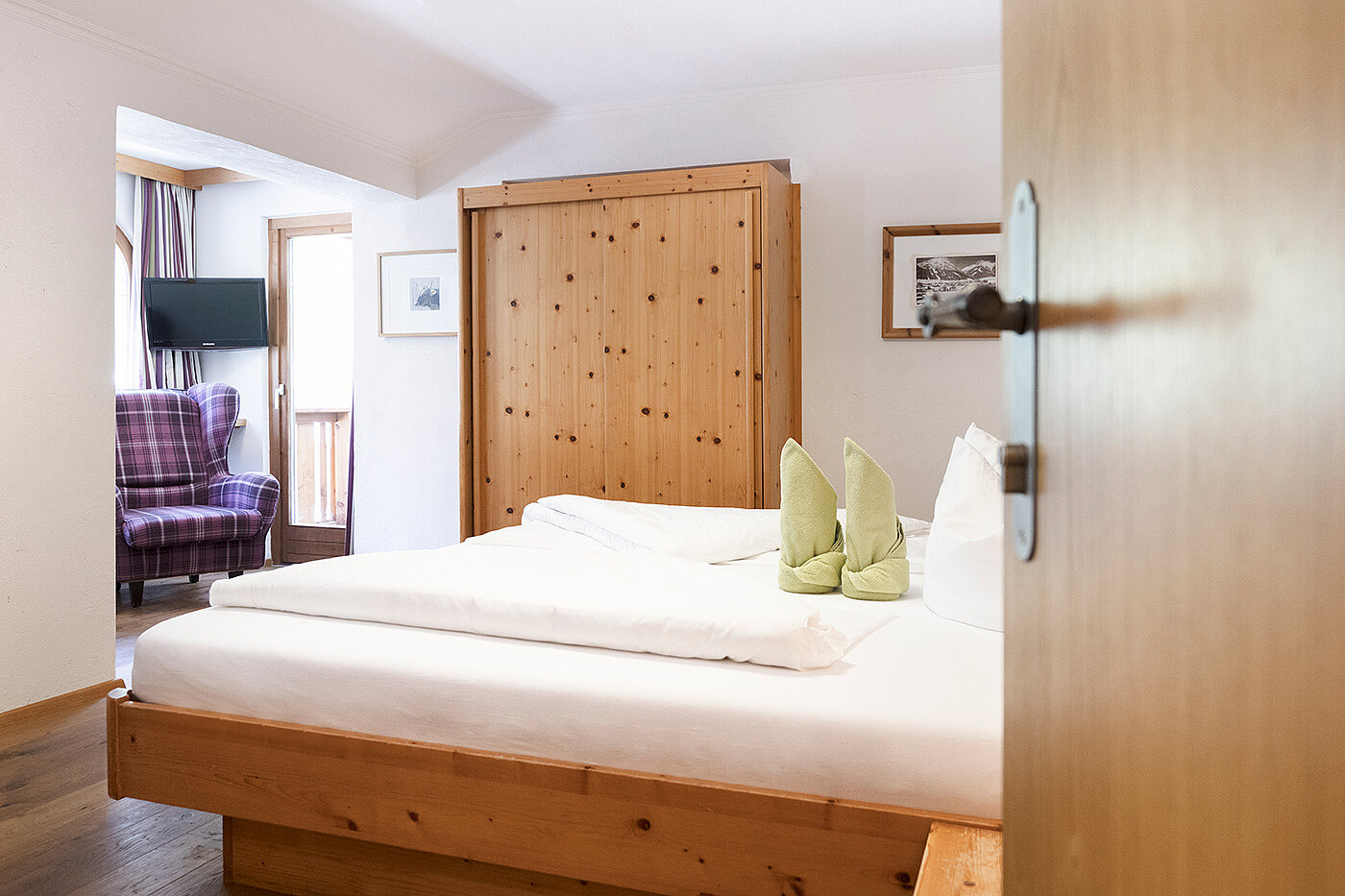 Ein gemütliches Schlafzimmer mit einem Holzbett, einem Kleiderschrank, ordentlich gefalteten Handtüchern und einem karierten Sessel am Fenster.