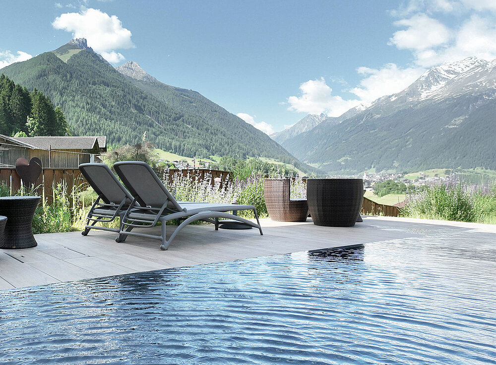 Von zwei Liegestühlen am Pool blicken Sie auf Berge und Grün unter einem blauen Himmel mit vereinzelten Wolken.