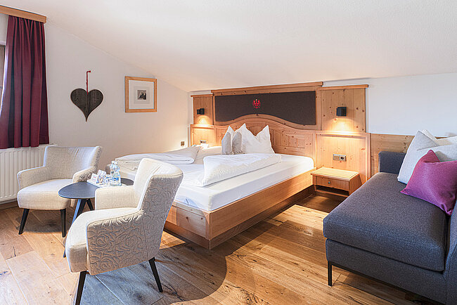 Gemütliches Hotelzimmer mit einem Doppelbett, zwei Sesseln, einem kleinen Tisch und einem Sofa, in neutralen Tönen gehalten.