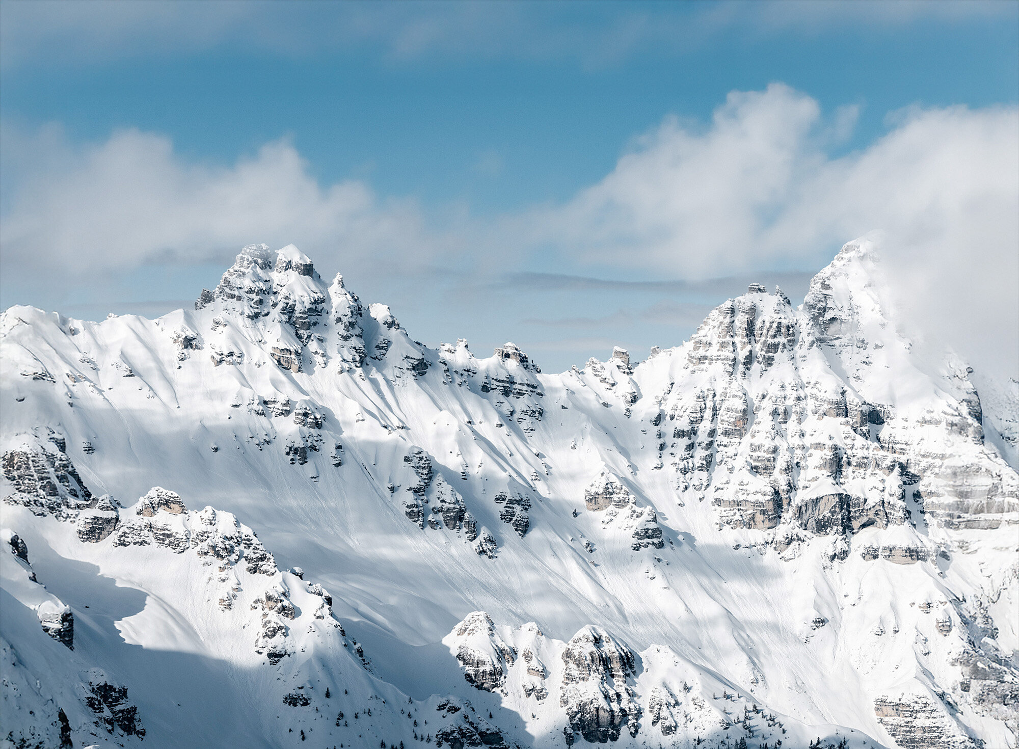 Schneebedeckte Berggipfel unter einem teilweise bewölkten blauen Himmel.