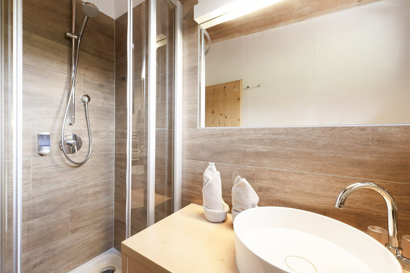 Modernes Badezimmer mit Holzakzenten, einem runden Waschbecken und einer verglasten Dusche mit Chromarmaturen.