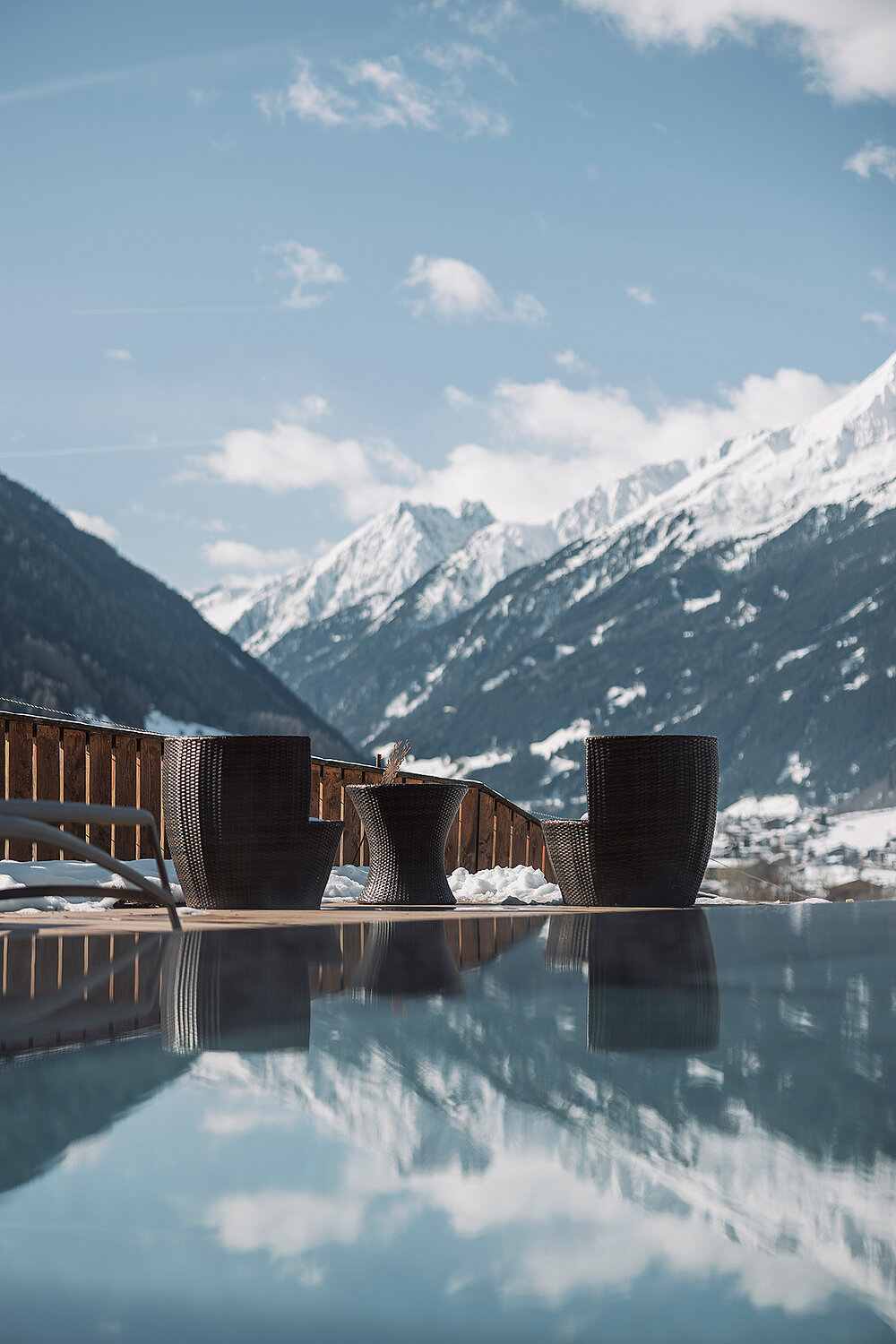 Außenaufnahme des Infinity-Pool mit Panoramablick in das Stubaital. Im Hintergrund sieht man den blau, leicht bewölkten, Himmel.