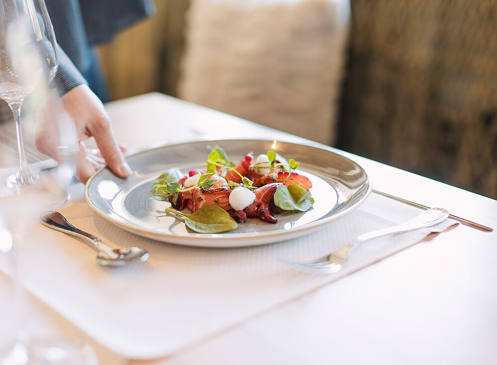 Eine Hand stellt einen Teller Salat mit Gemüse, Tomaten und Mozzarella auf einen Restauranttisch.