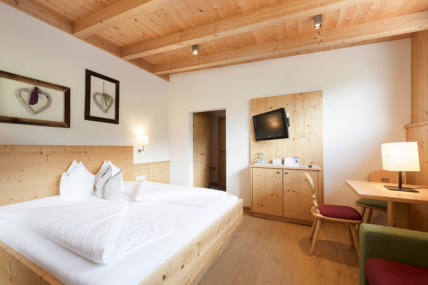 Gemütliches Hotelzimmer mit Doppelbett, Holzmöbeln, Wandkunst, Schreibtisch und Wandfernseher.