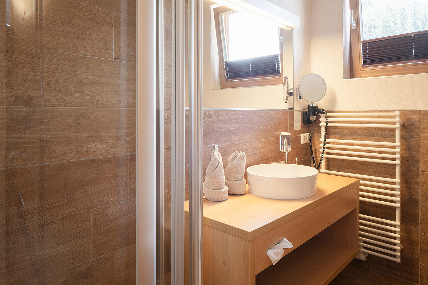 Modernes Badezimmer mit Holzakzenten, einem Aufsatzwaschbecken, einem Handtuchhalter und zwei ordentlich gefalteten Handtüchern auf der Ablage.
