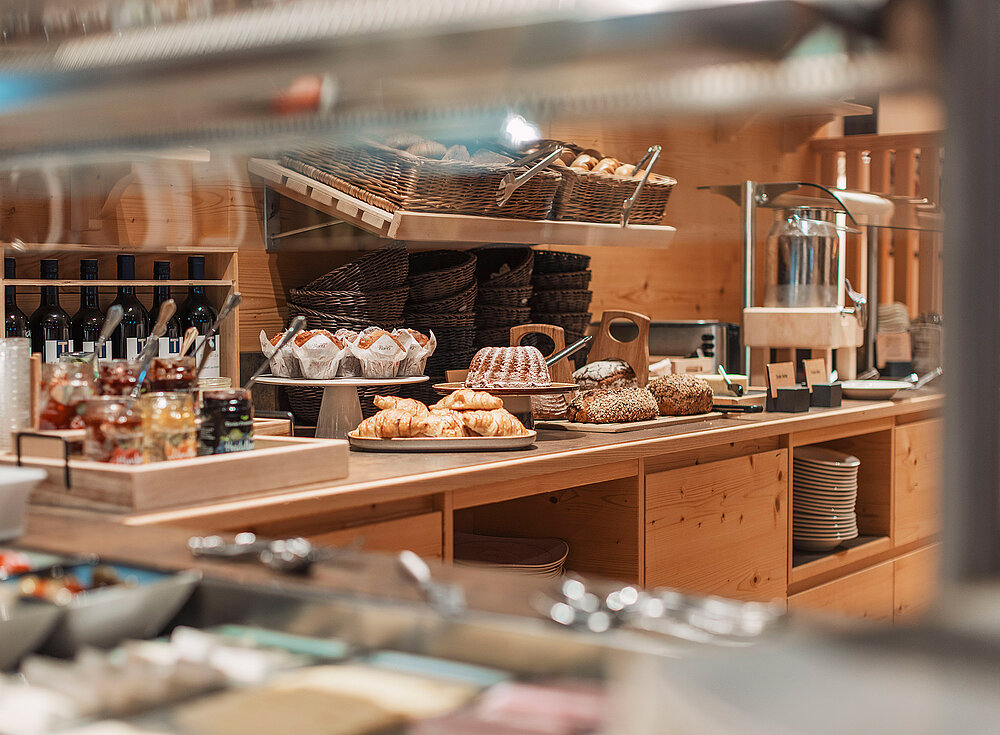 A person serves pastries on a plate using a cake tong in a warmly lit kitchen or bakery.