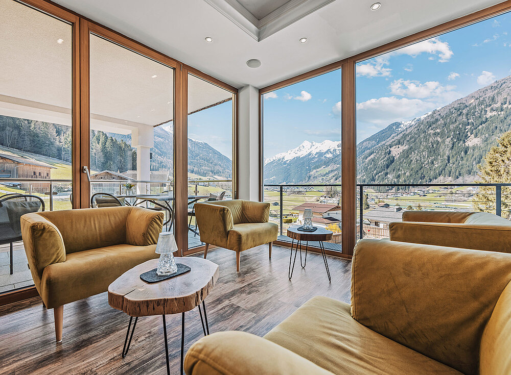 Moderne Lounge mit senffarbenen Stühlen, Marmortischen, großen Fenstern und Blick auf die Berge und ein sonniges Tal draußen.