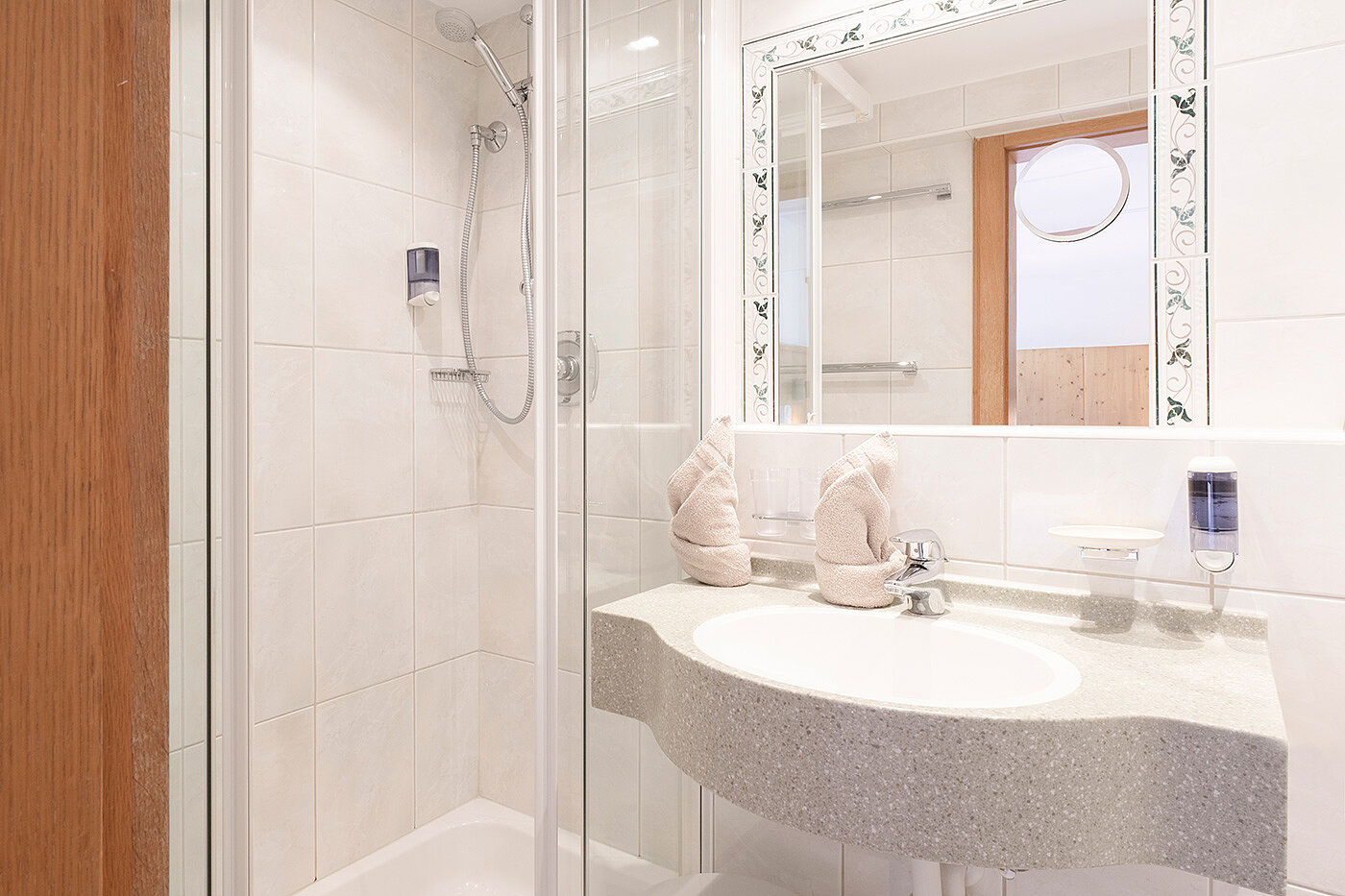 Kleines, modernes Badezimmer mit Glasdusche, weißem Waschbecken, großem Spiegel und ordentlich gefalteten Handtüchern auf der Ablage.