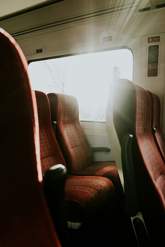 Sonnenlicht strömt durch ein Fenster und beleuchtet leere rote Sitze im Inneren eines Eisenbahnwaggons.