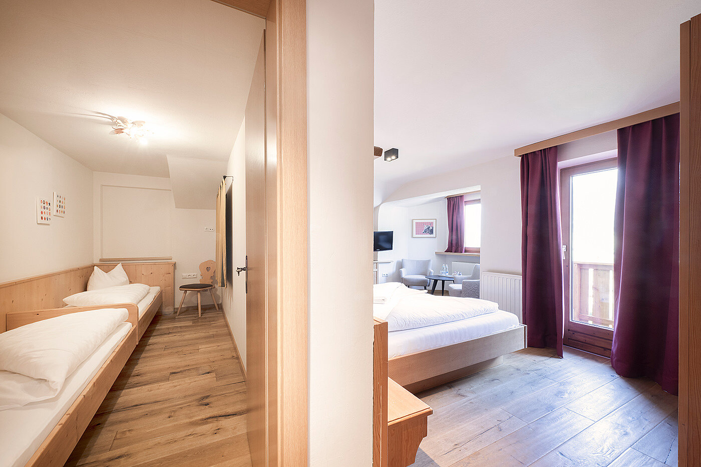 Hotelsuite mit zwei separaten Schlafbereichen, jeweils mit Einzel- oder Doppelbetten, Holzböden und Tageslicht.